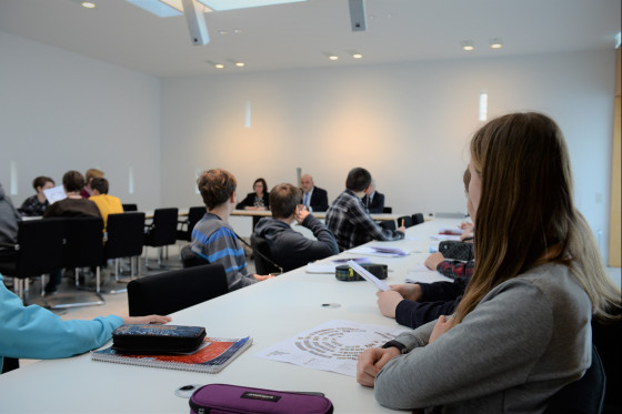 Schülerinnen und Schüler tauschen sich in einem Sitzungssaal mit Abgeordneten aus.